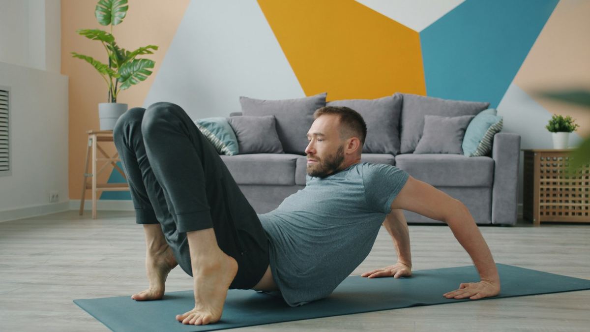 Homme sur un tapis de yoga dans son salon, genoux pliés, en position de départ du pont