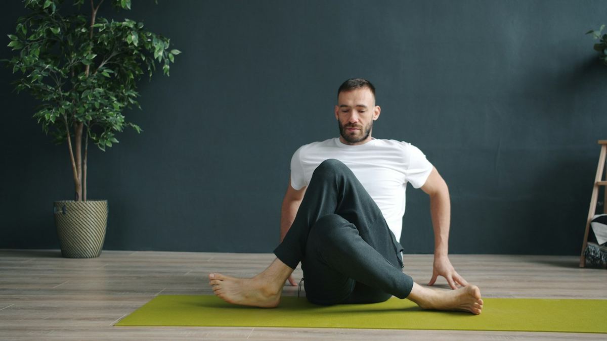 Homme assis sur un tapis d'exercice, une jambe croisée par-dessus l'autre, le buste en rotation