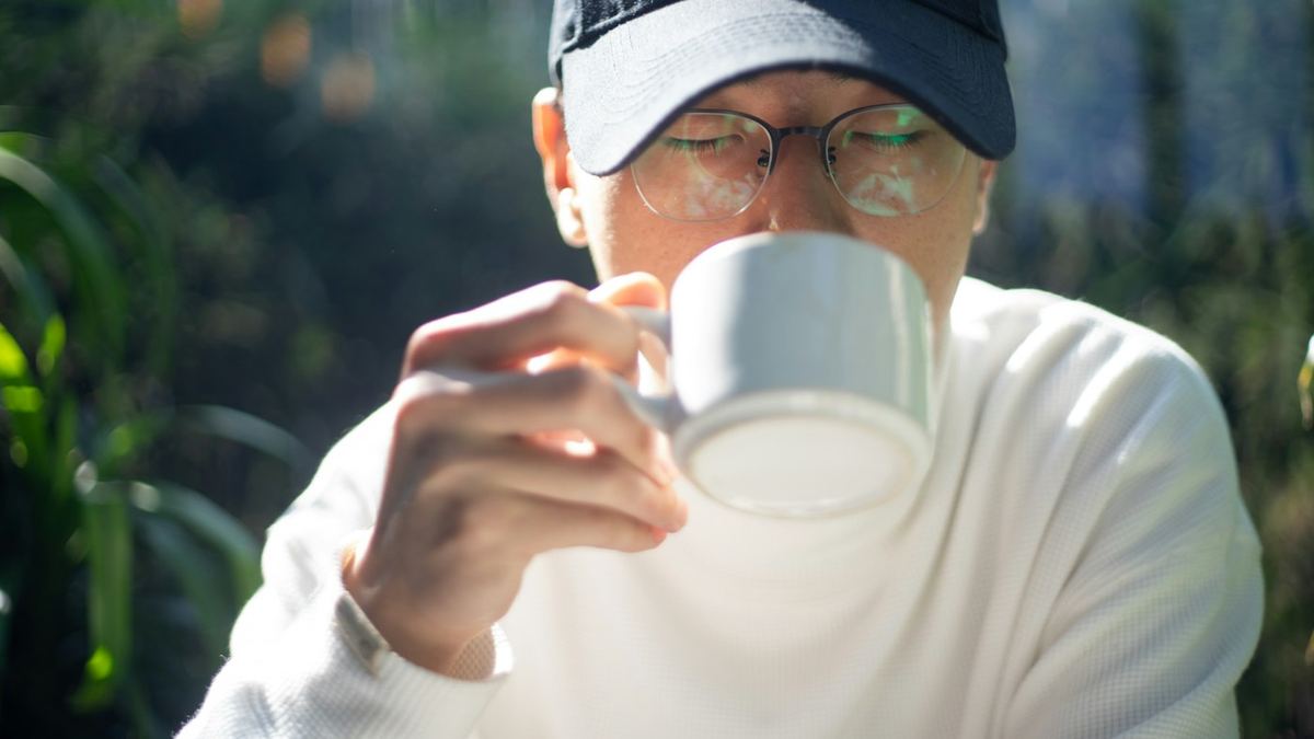 Homme en casquette et lunettes buvant dans une tasse blanche en extérieur